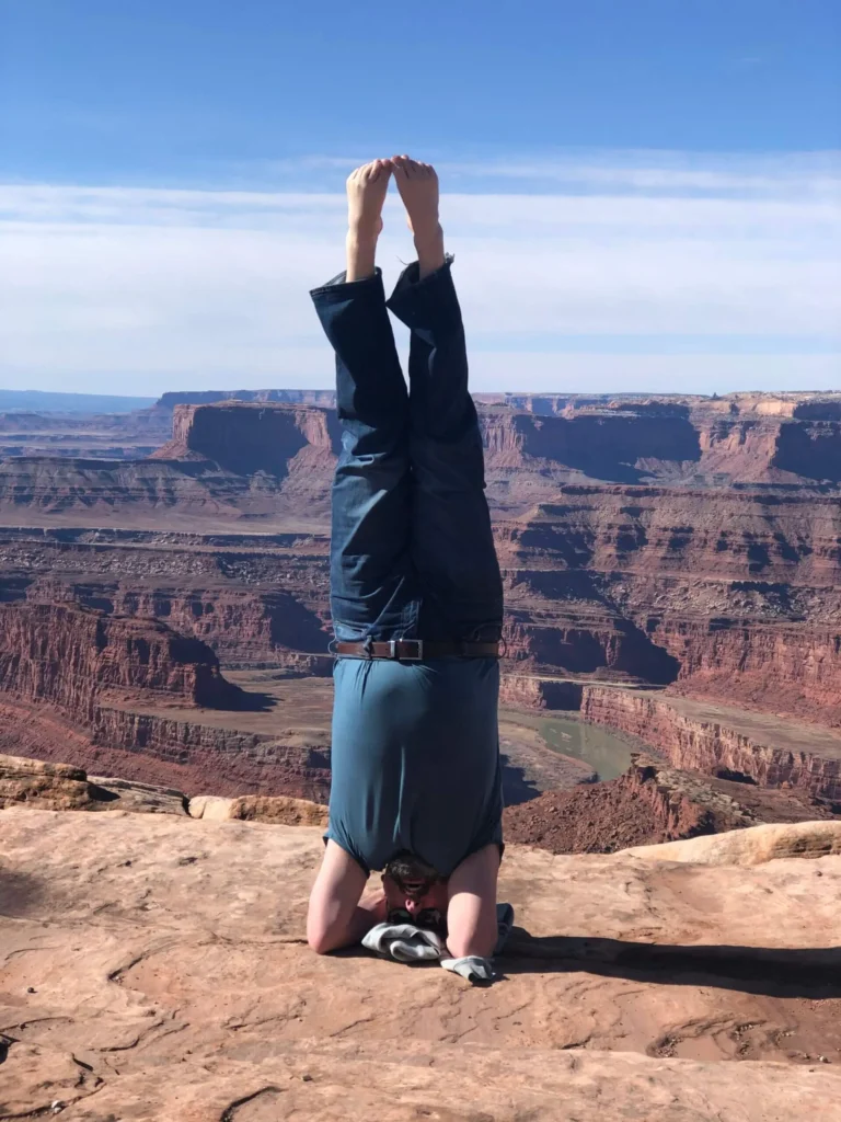 Person doing a headstand on a cliff overlooking a canyon.