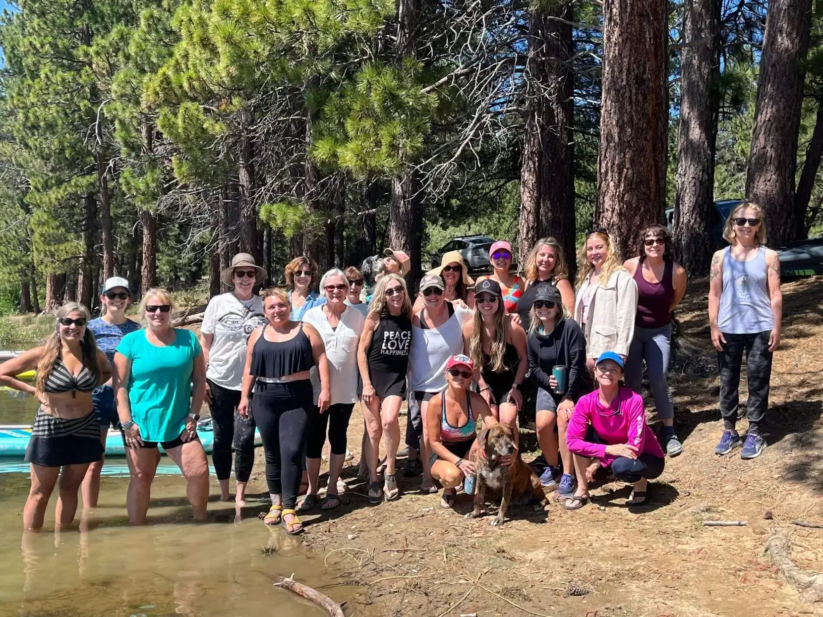 Group of people posing near a lake surrounded by trees on a sunny day.